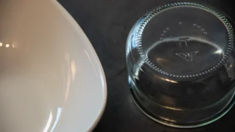 Sauberes Geschirr wie ein glänzendes Glas und ein weißer Teller auf einer eleganten, dunklen Oberfläche platziert.