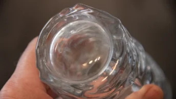 A hand holds a clean glass, showcasing the spotless glassware bottom for ultimate kitchen sparkle.